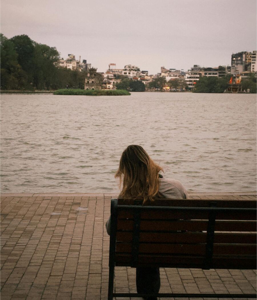 A person sitting alone on a bench, looking out over a lake at the city on the far shore